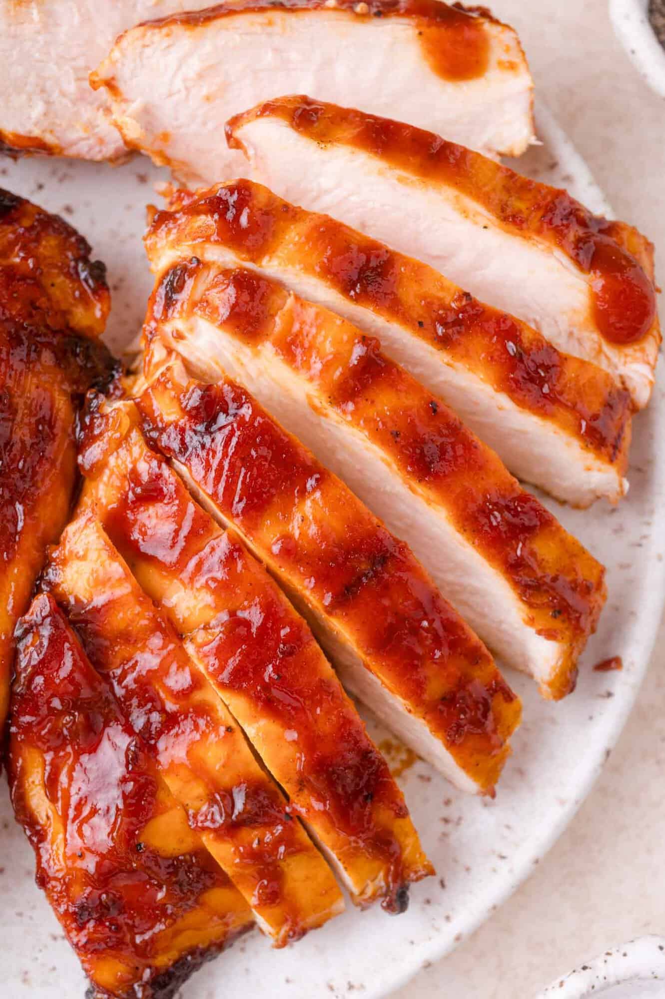 Sliced grilled chicken breast with a reddish-brown barbecue sauce arranged on a white plate.