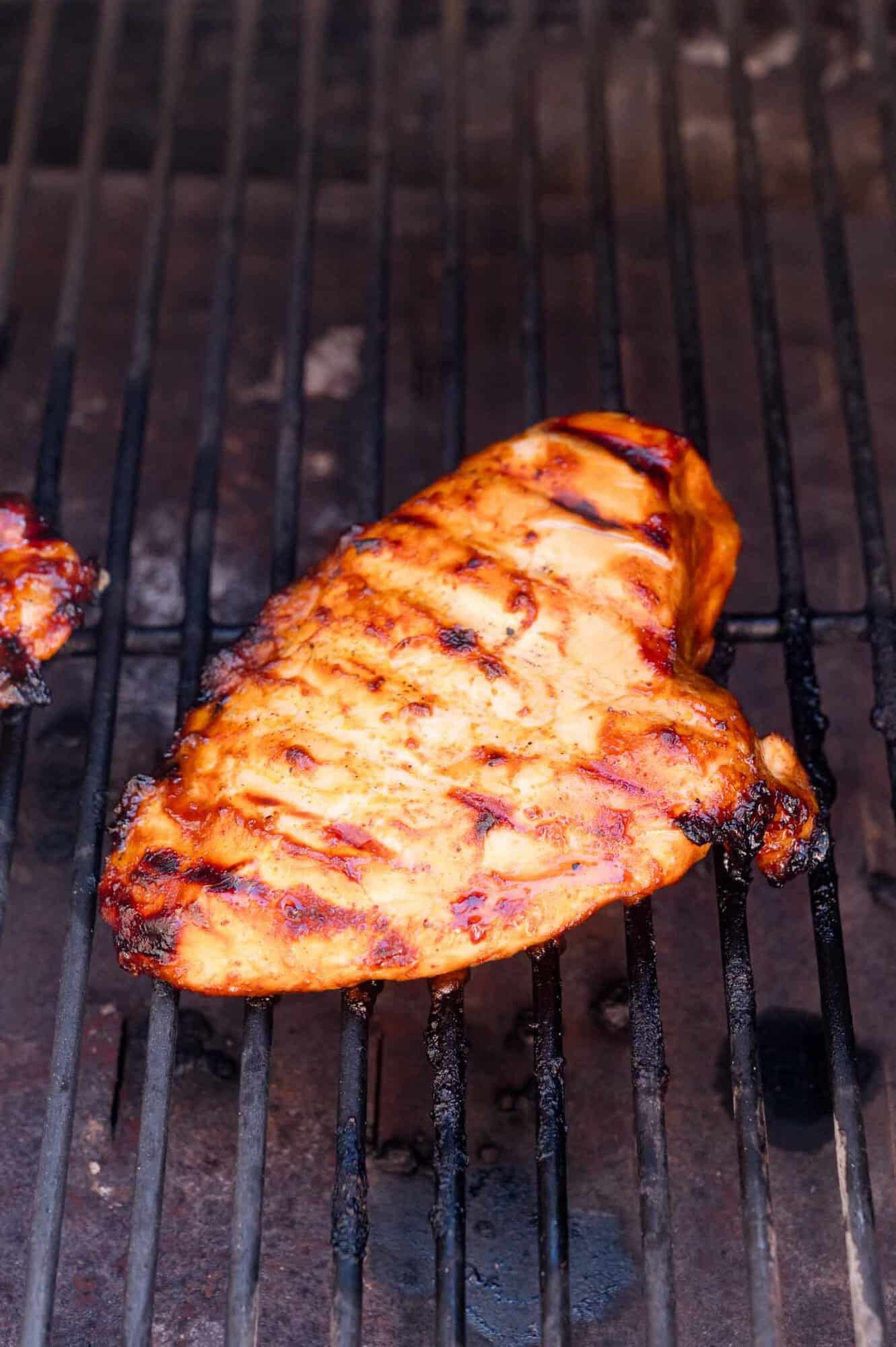 A grilled chicken breast with visible char marks cooking on a barbecue grill.