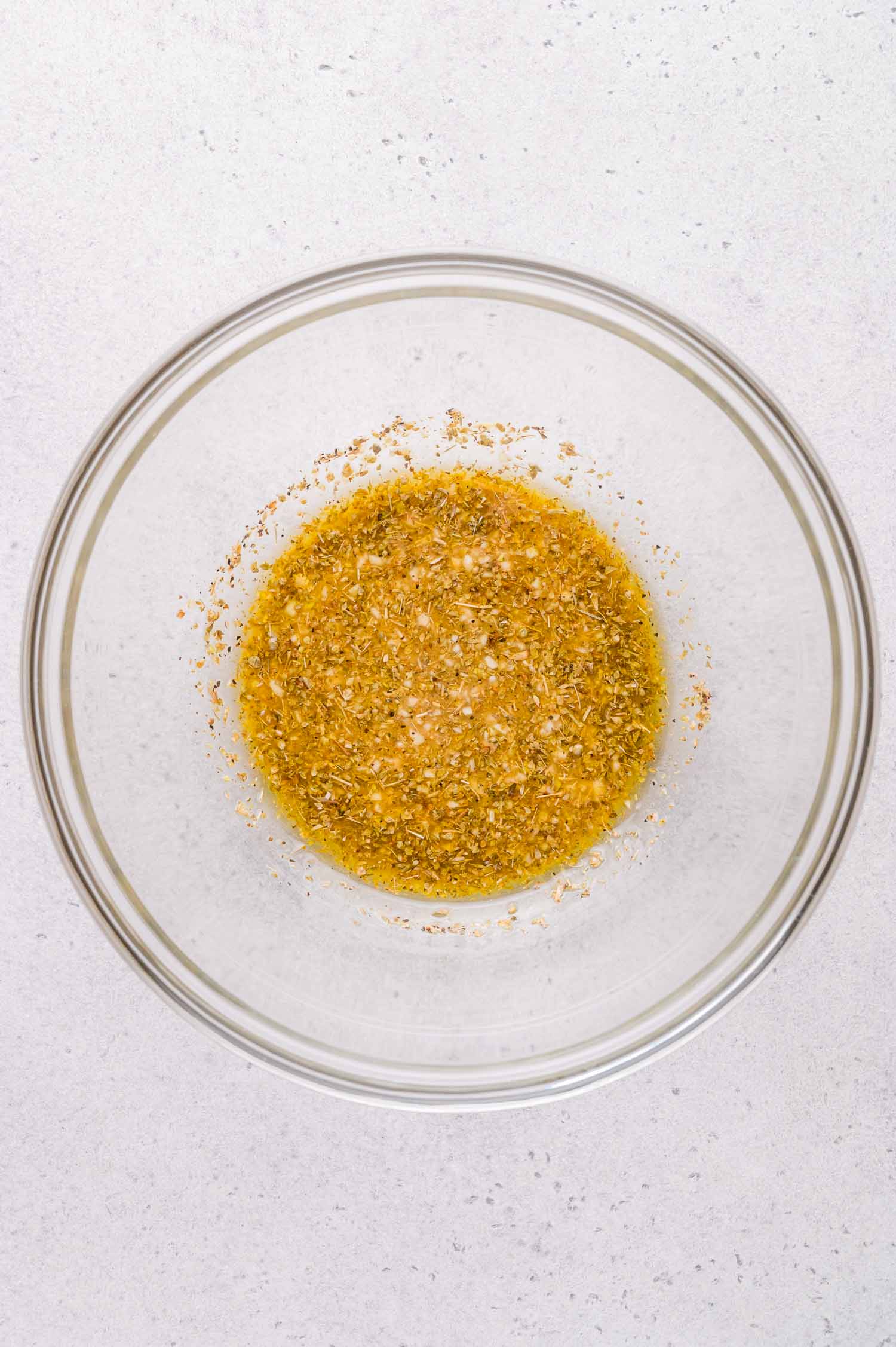A clear glass bowl containing a marinade mixture on a light-colored countertop.
