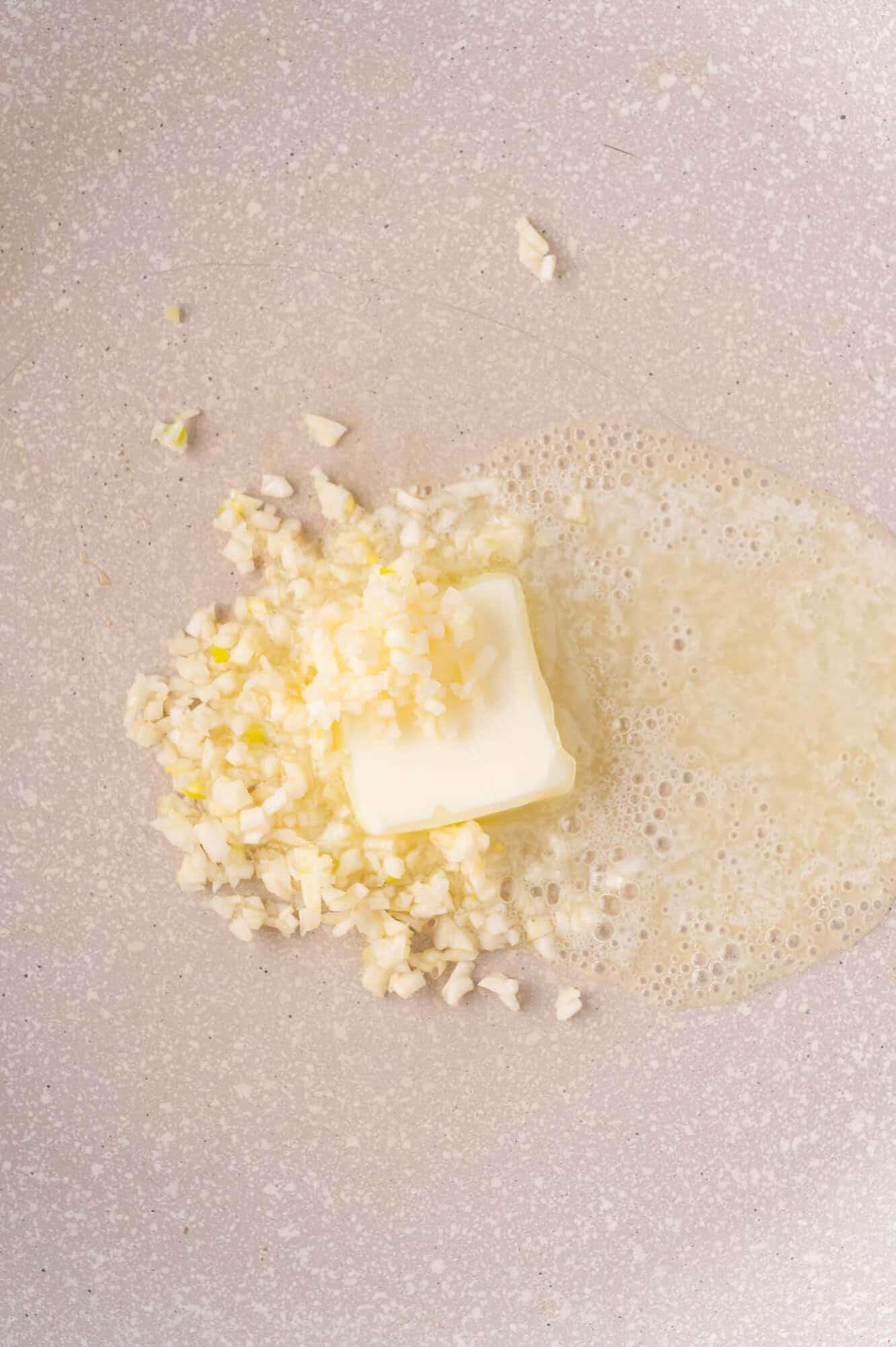 Finely chopped garlic and a pat of butter melting in a light-colored pan.