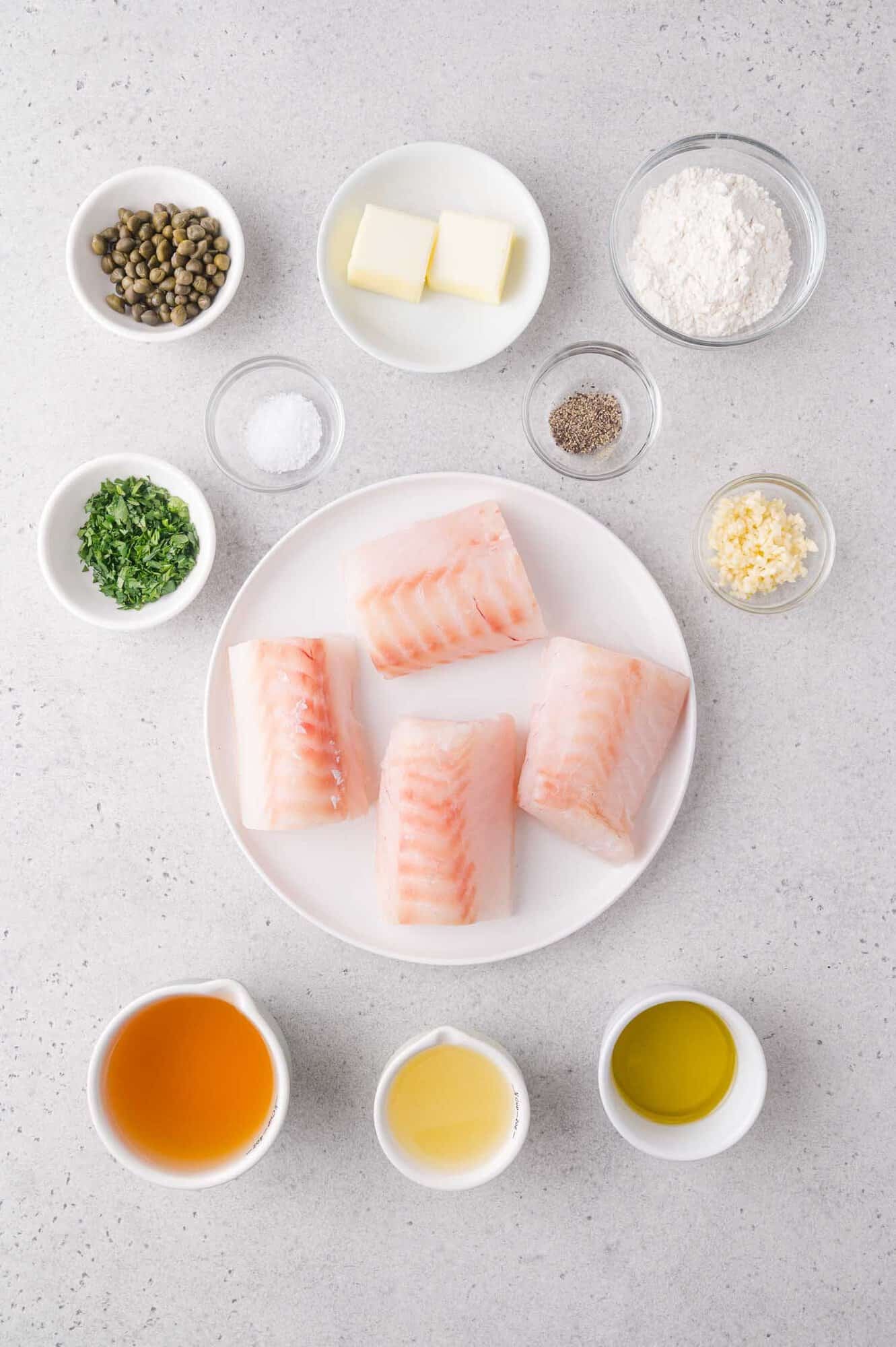 Four raw cod fillets on a plate surrounded by small bowls containing capers, butter, flour, salt, pepper, chopped herbs, minced garlic, broth, wine, and olive oil.