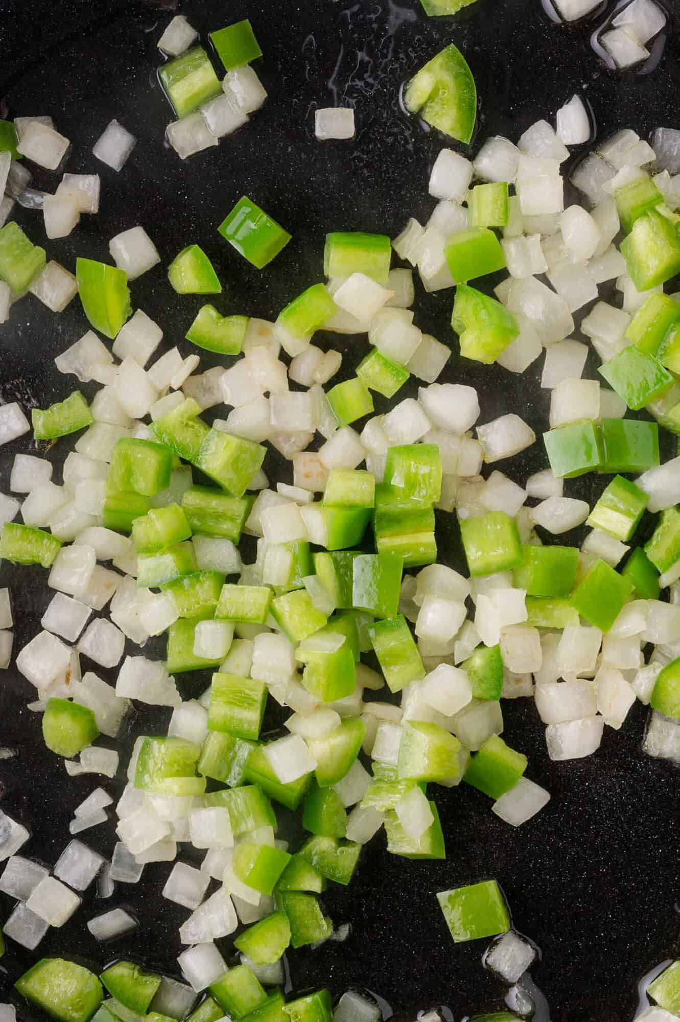 Diced jalapeno peppers and onions cooking in a pan.