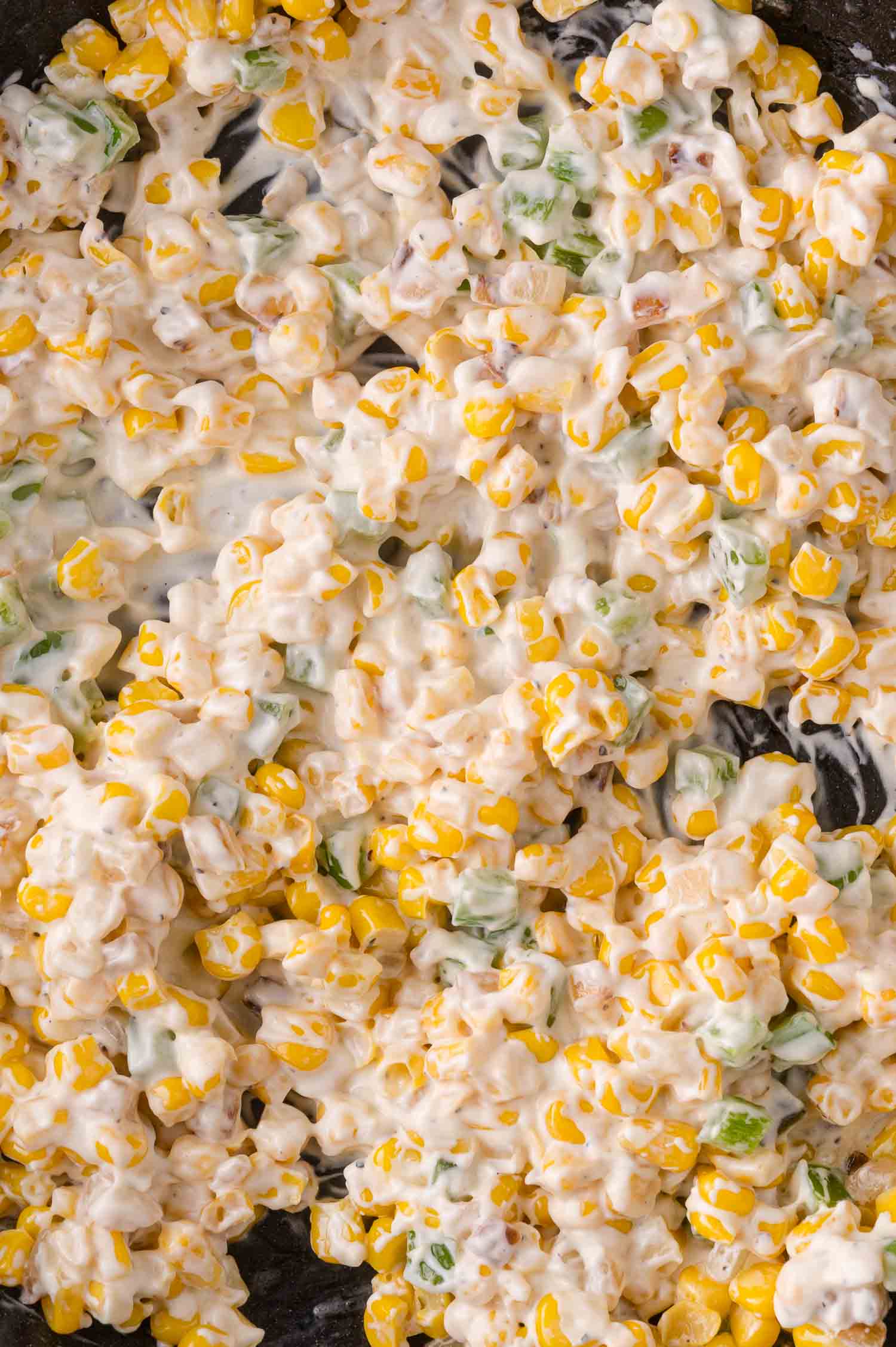 Close-up of creamy corn mixed with diced peppers and onions.