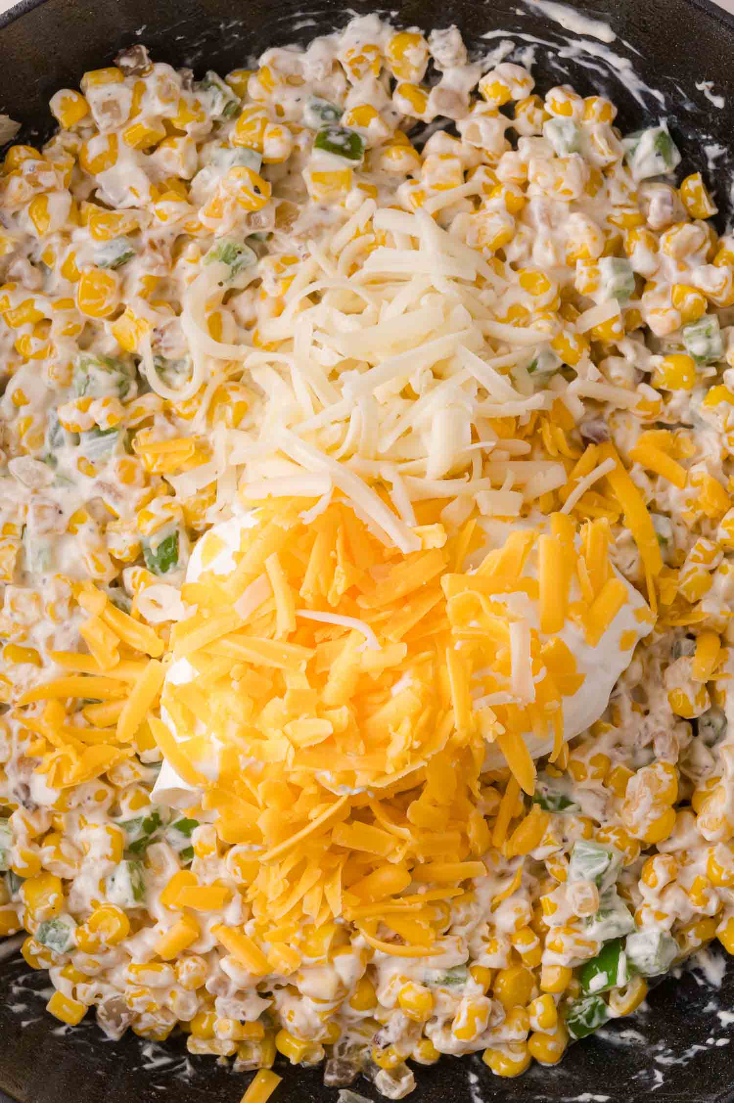 Close-up of a creamy corn mixture topped with shredded white and yellow cheese in a pan.