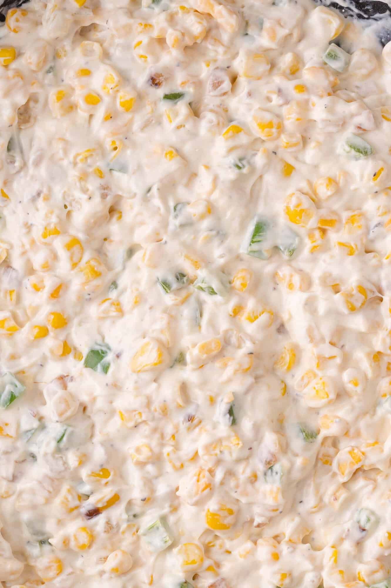 Close-up of a creamy corn dip with visible corn kernels and jalapeno peppers mixed in a white sauce.
