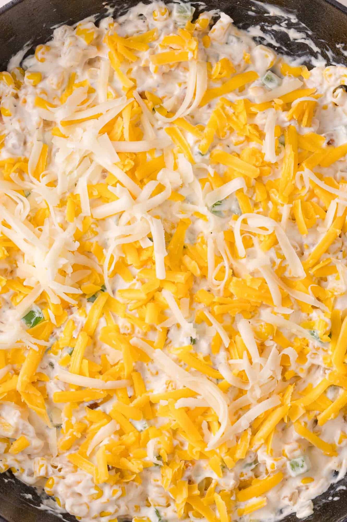 A close-up of a creamy dip mixture topped with shredded yellow and white cheese in a pan.