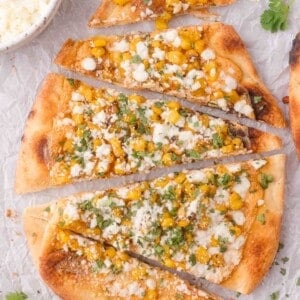Flatbread topped with corn, crumbled cheese, and chopped cilantro, sliced into pieces and arranged on parchment paper.