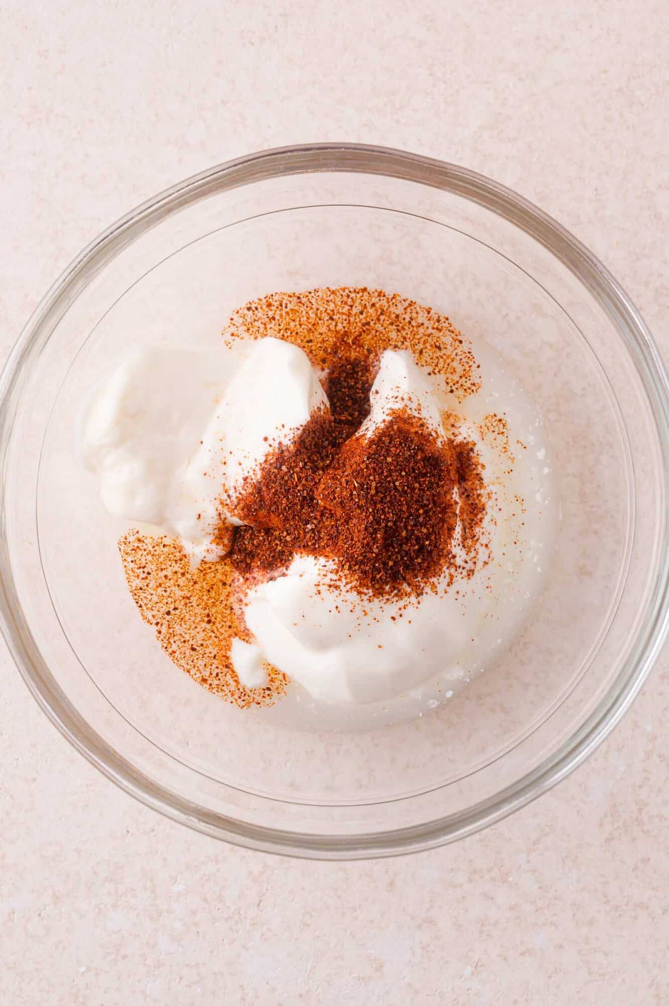 A clear glass bowl contains sour cream, chili powder, and lime juice.