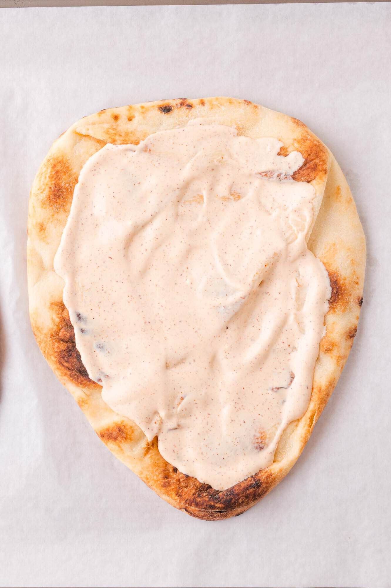 Flatbread spread evenly over the surface with a rich, creamy white sauce and placed on a white cookie sheet.