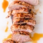 Sliced roasted pork tenderloin with a browned, seasoned crust and juices on a white surface.