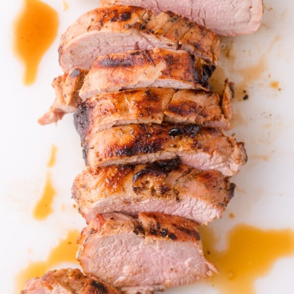 Sliced roasted pork tenderloin with a browned, seasoned crust and juices on a white surface.