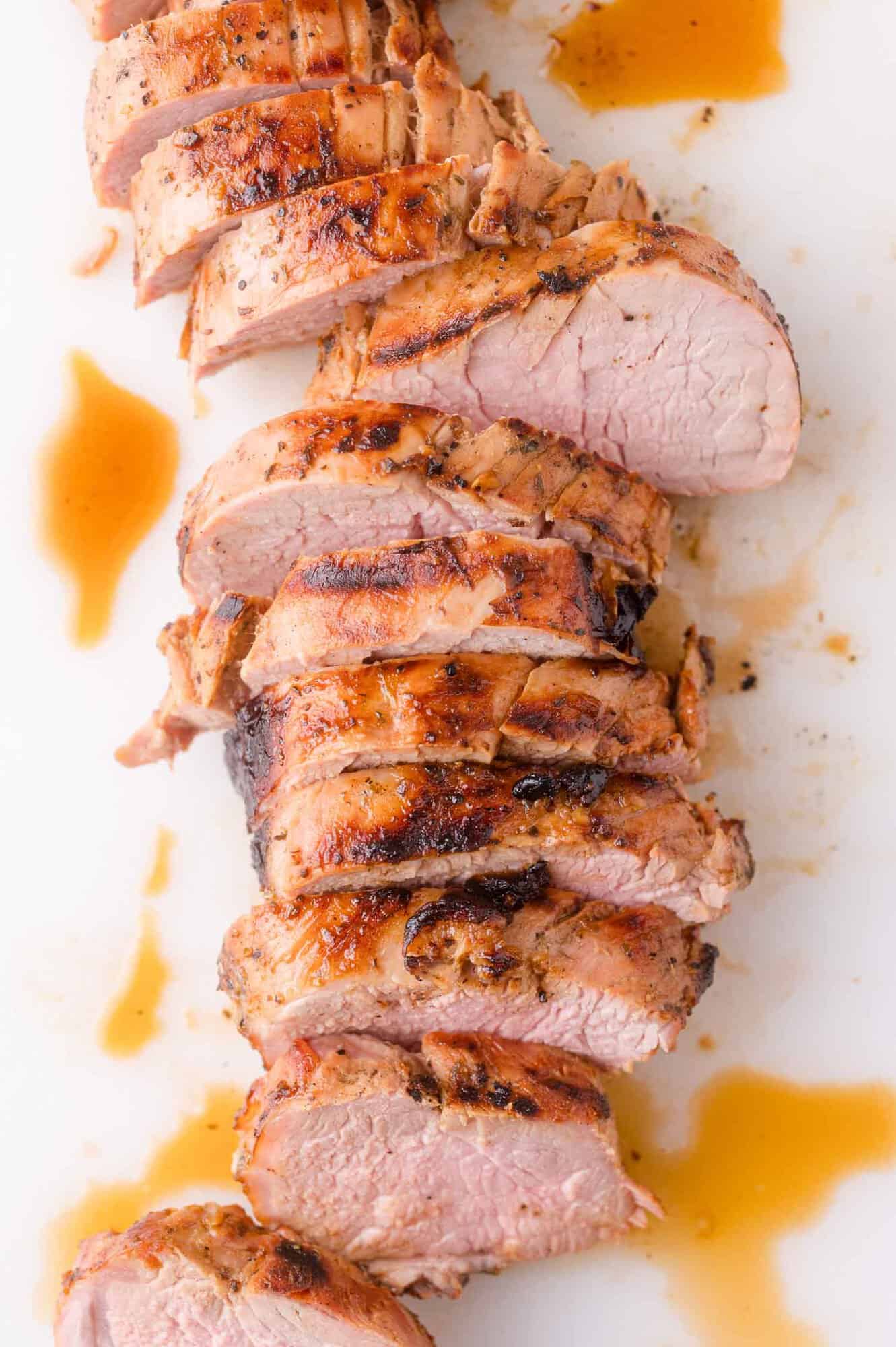 Sliced cooked pork tenderloin with grill marks, arranged on a white surface with a drizzle of brown sauce.