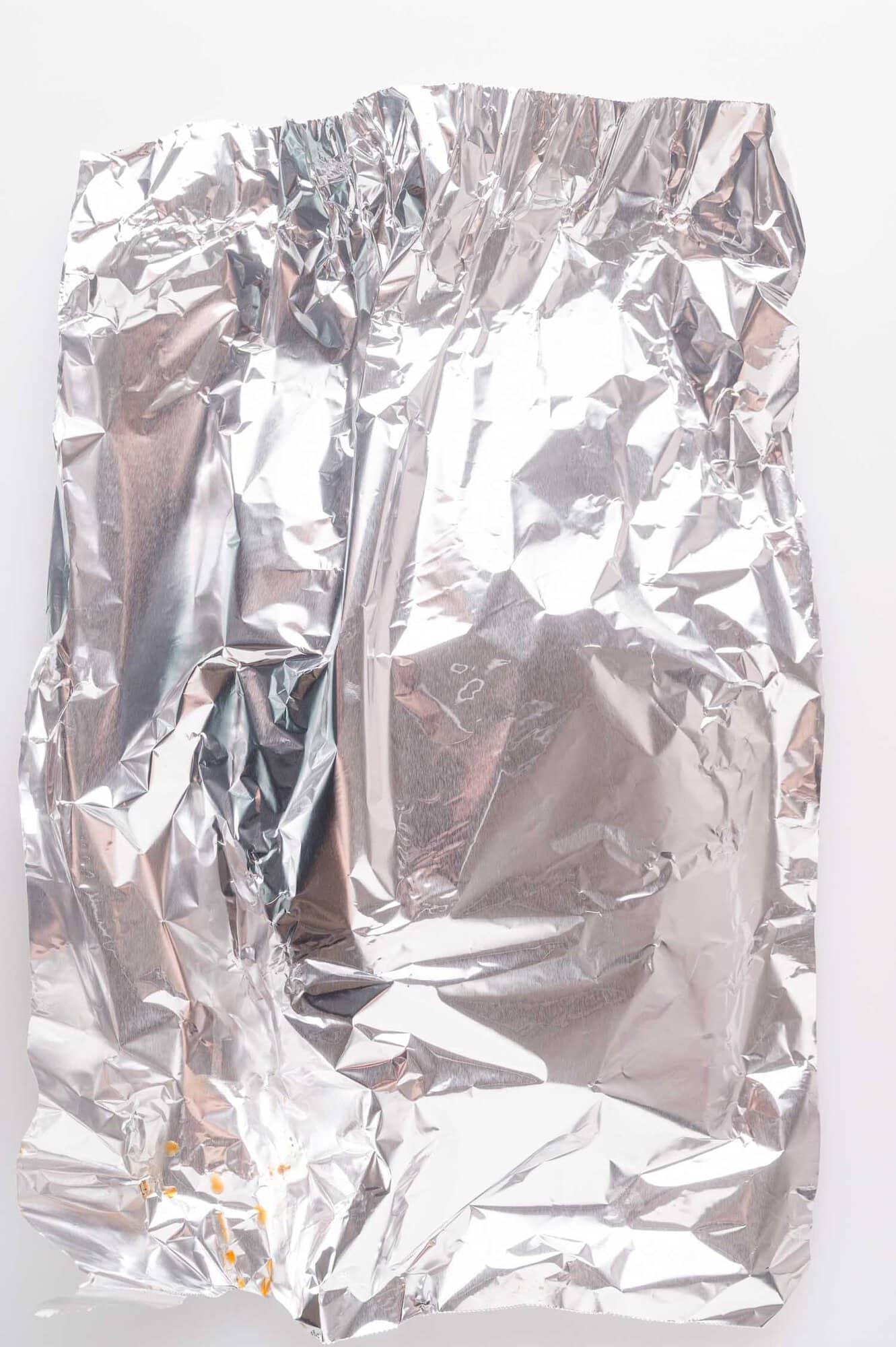 A crumpled sheet of aluminum foil with a few small orange crumbs on a white background.