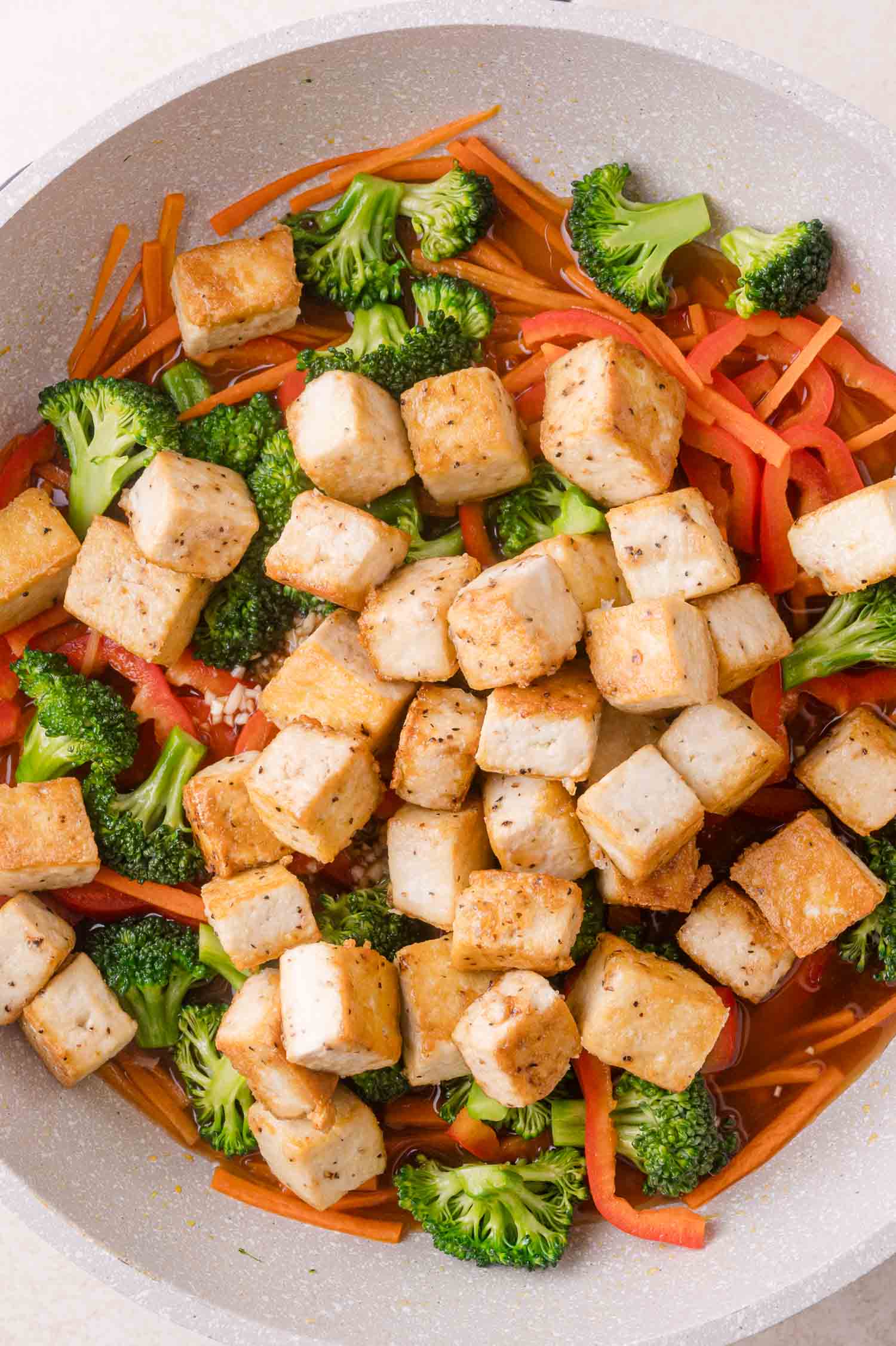 A pan filled with cooked tofu cubes, broccoli florets, sliced red bell pepper, and julienned carrots.
