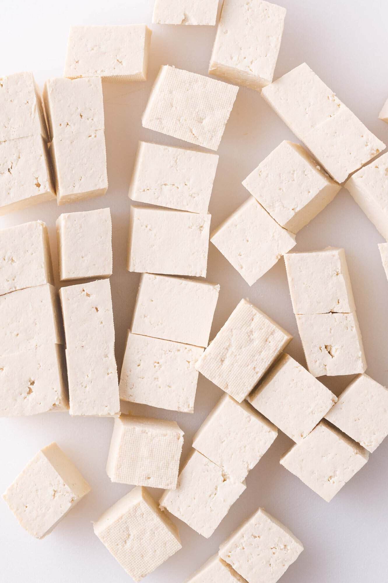 Cubes of plain tofu arranged on a white surface.
