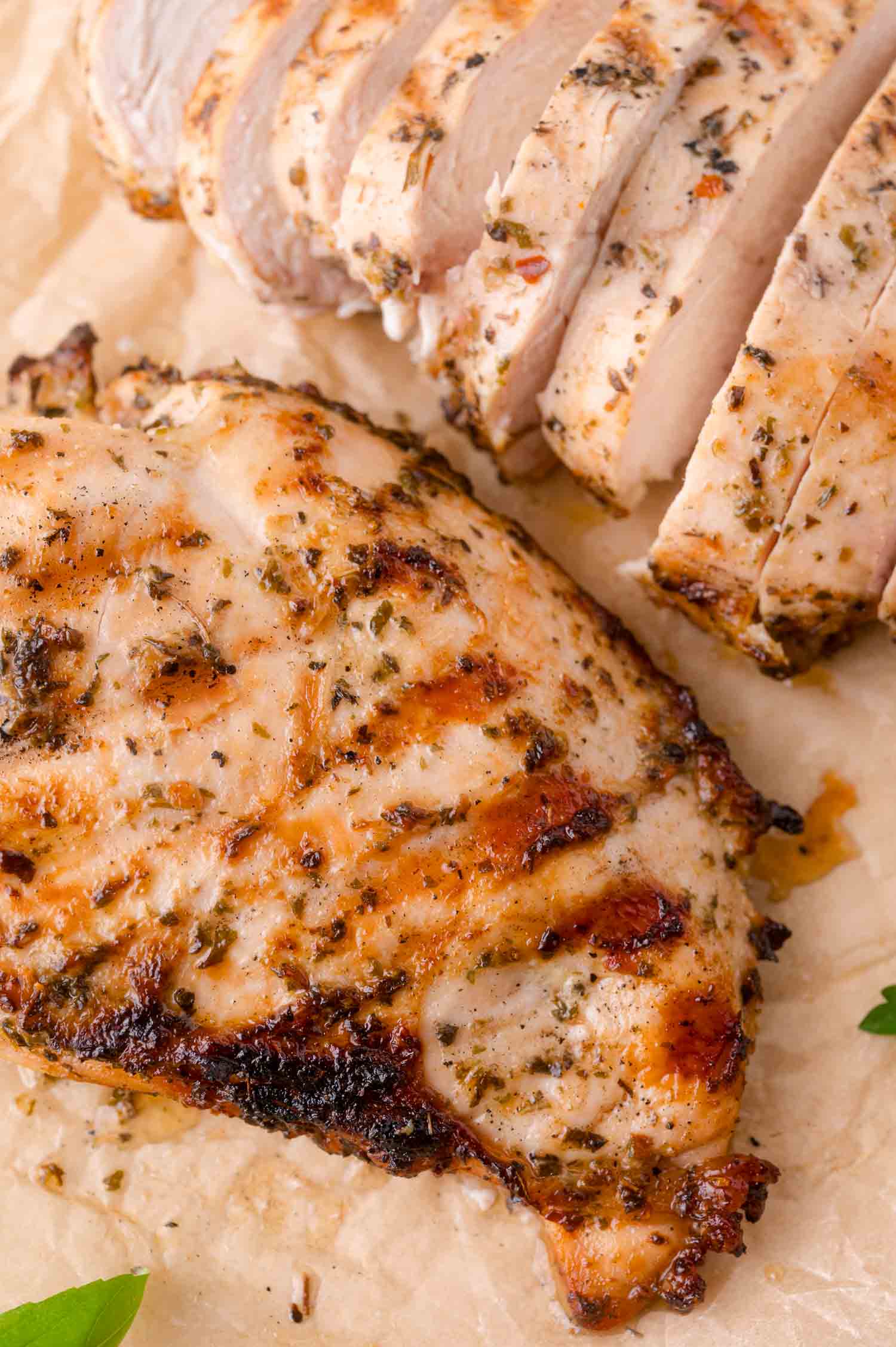 Grilled, seasoned chicken breast and sliced chicken breast on parchment paper.