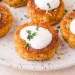 Close-up of golden brown crab cakes topped with a dollop of white aioli and garnished with chopped fresh herbs on a speckled plate.