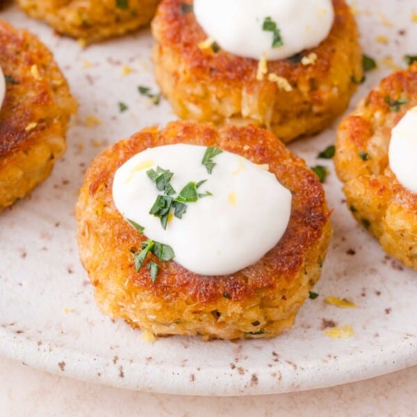 Close-up of golden brown crab cakes topped with a dollop of white aioli and garnished with chopped fresh herbs on a speckled plate.