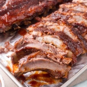 A tray of sliced, cooked barbecue ribs with a glossy, saucy coating, displayed on a metal baking sheet.