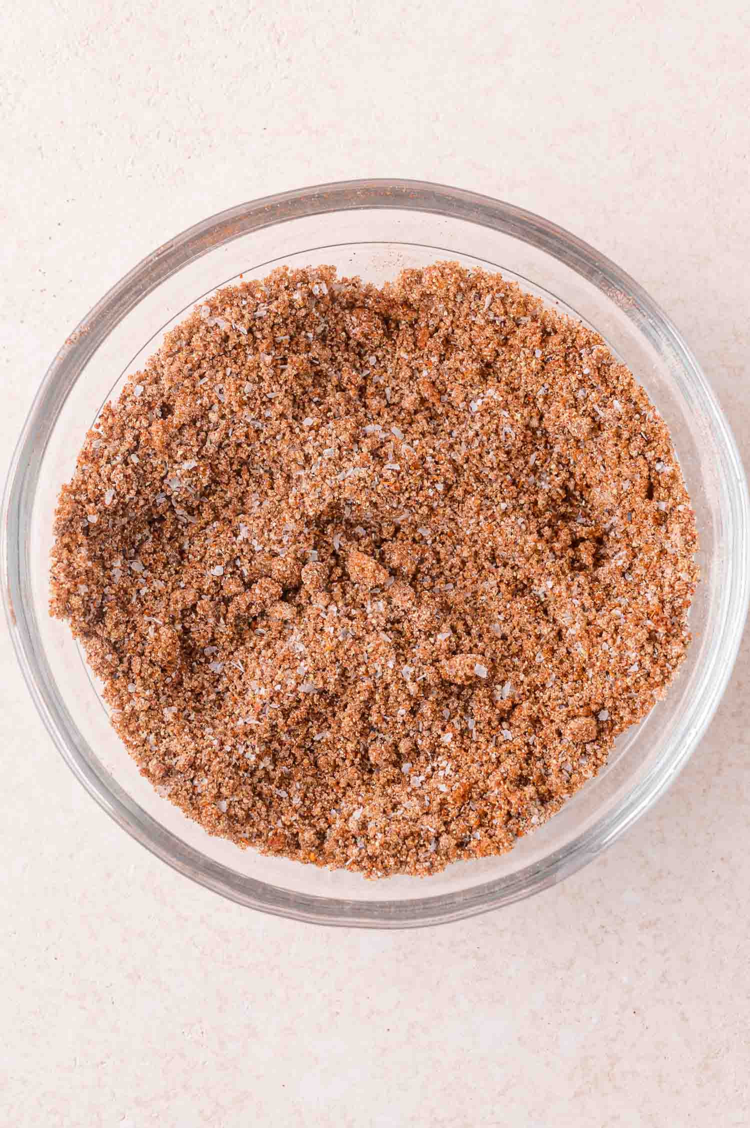 A clear glass bowl filled with a mixture of brown and white dry seasoning or spice blend, placed on a light-colored surface.