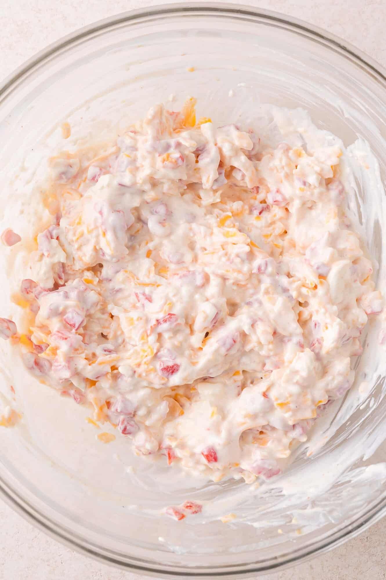 A glass bowl filled with a creamy pimento cheese dip.