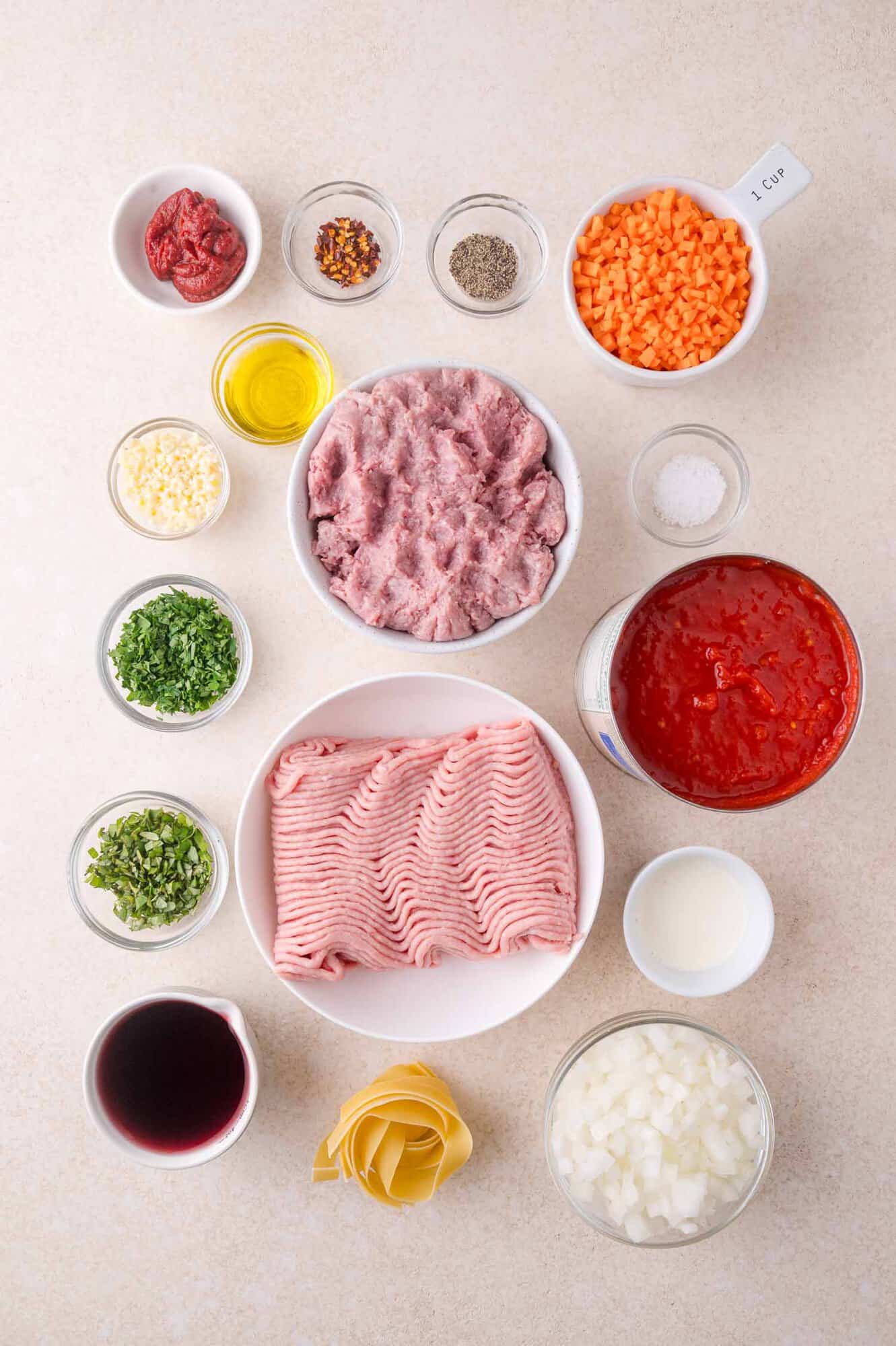 Ingredients for a pasta dish arranged on a countertop, including ground meat, tomato sauce, vegetables, herbs, spices, olive oil, cream, and lasagna noodles in separate bowls.