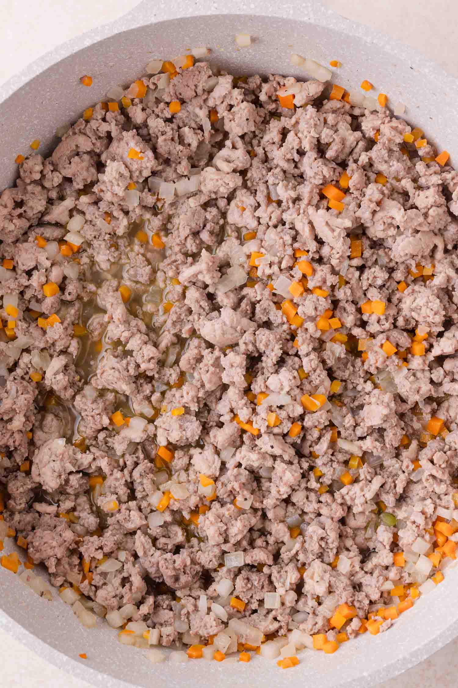 Cooked ground turkey and Italian sausage mixed with finely chopped onions and carrots in a pan.