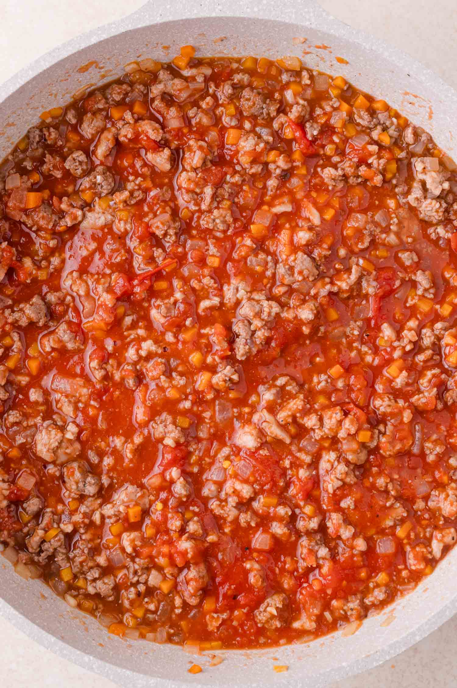 A close-up of a pan filled with ground meat and tomato sauce mixed with diced vegetables, resembling a simmering meat sauce or Bolognese.