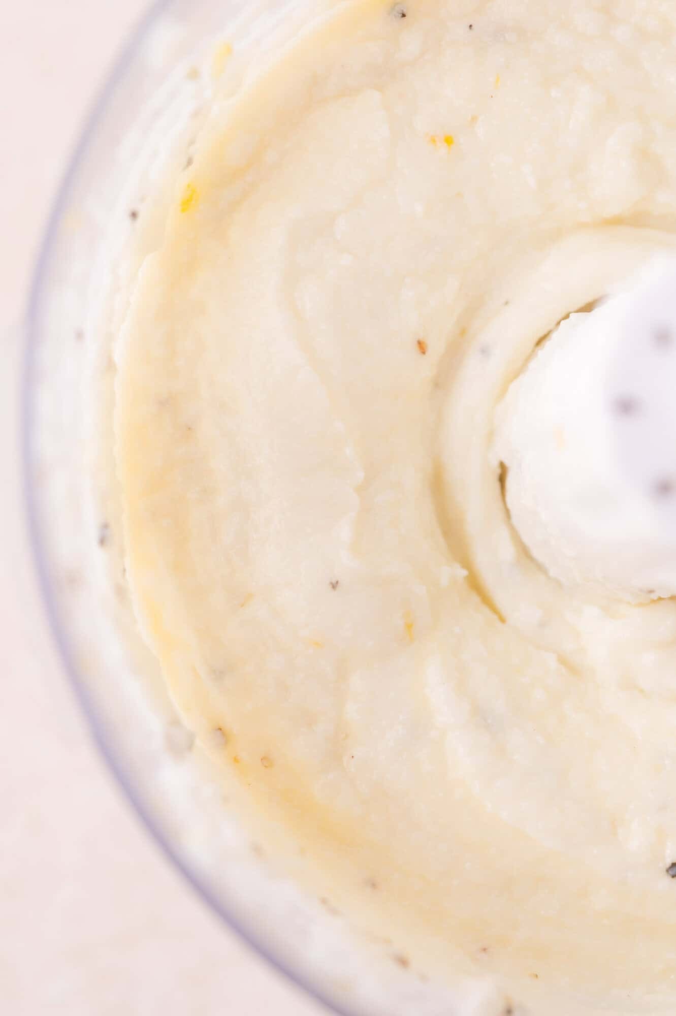 Close-up of smooth, creamy mixture being blended in a food processor, with visible flecks of seasoning throughout.
