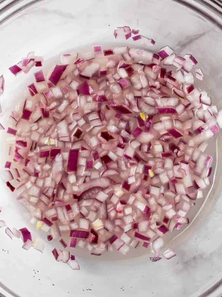 Onions in lime juice in a clear glass bowl.