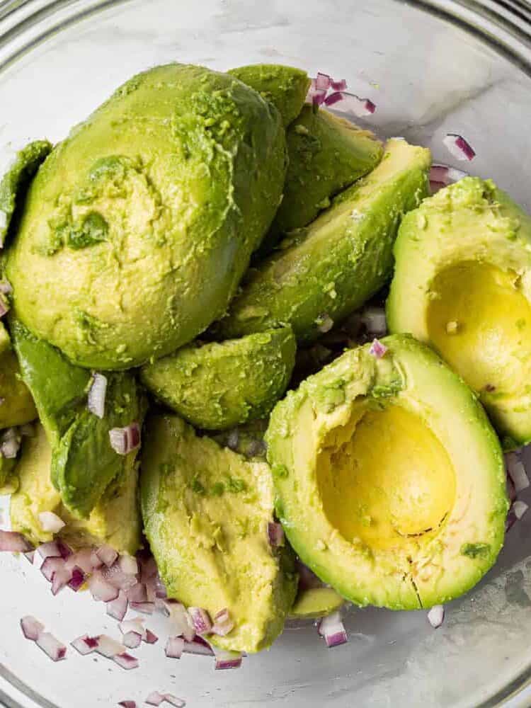 Peeled avocado halves in a bowl with red onions.