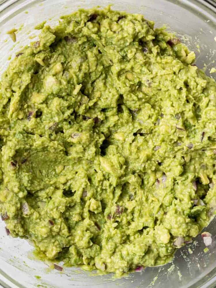 Mashed avocado in a clear glass bowl.