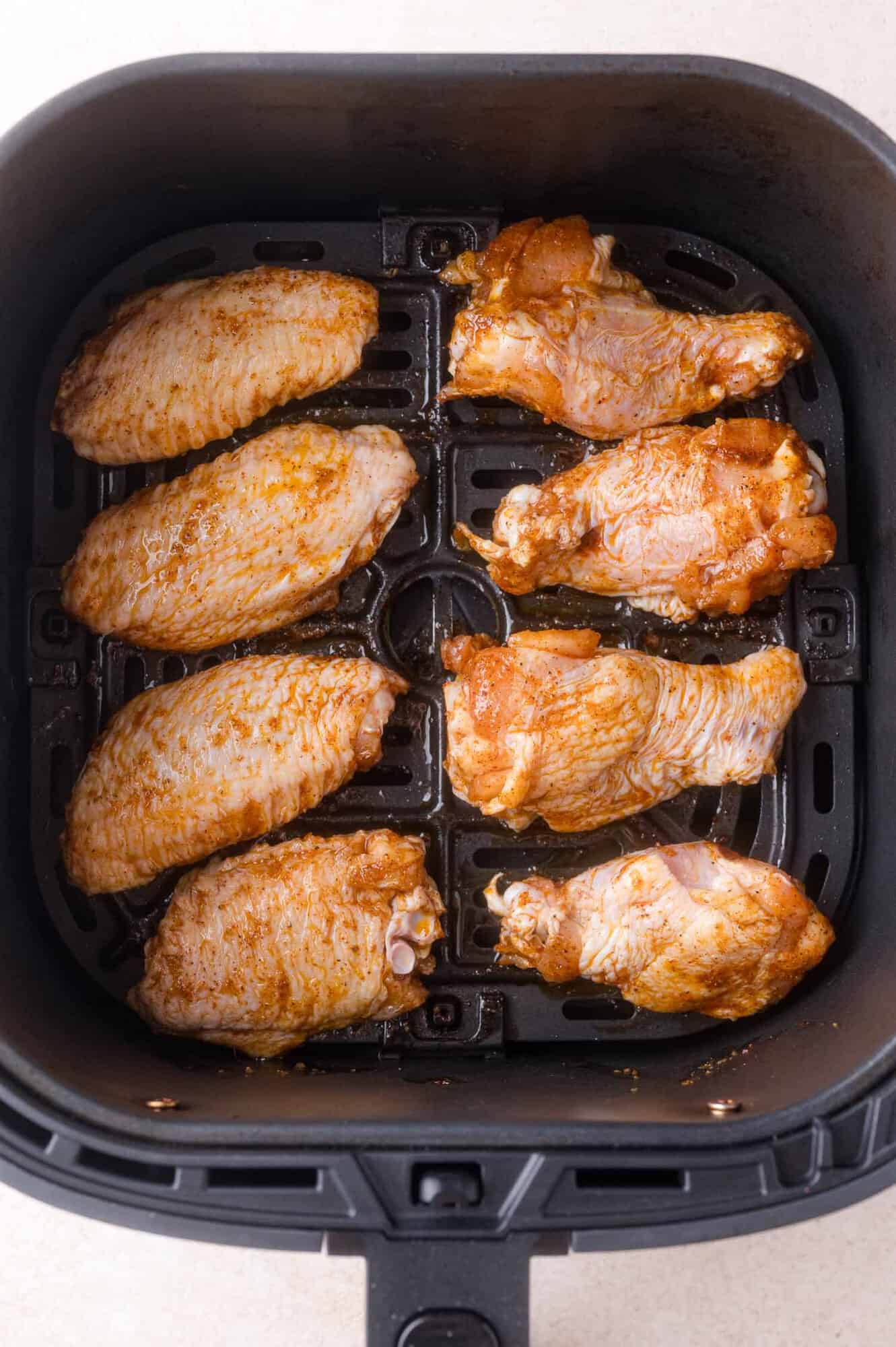 Eight seasoned chicken wings are arranged in a single layer inside an air fryer basket, ready to be cooked.