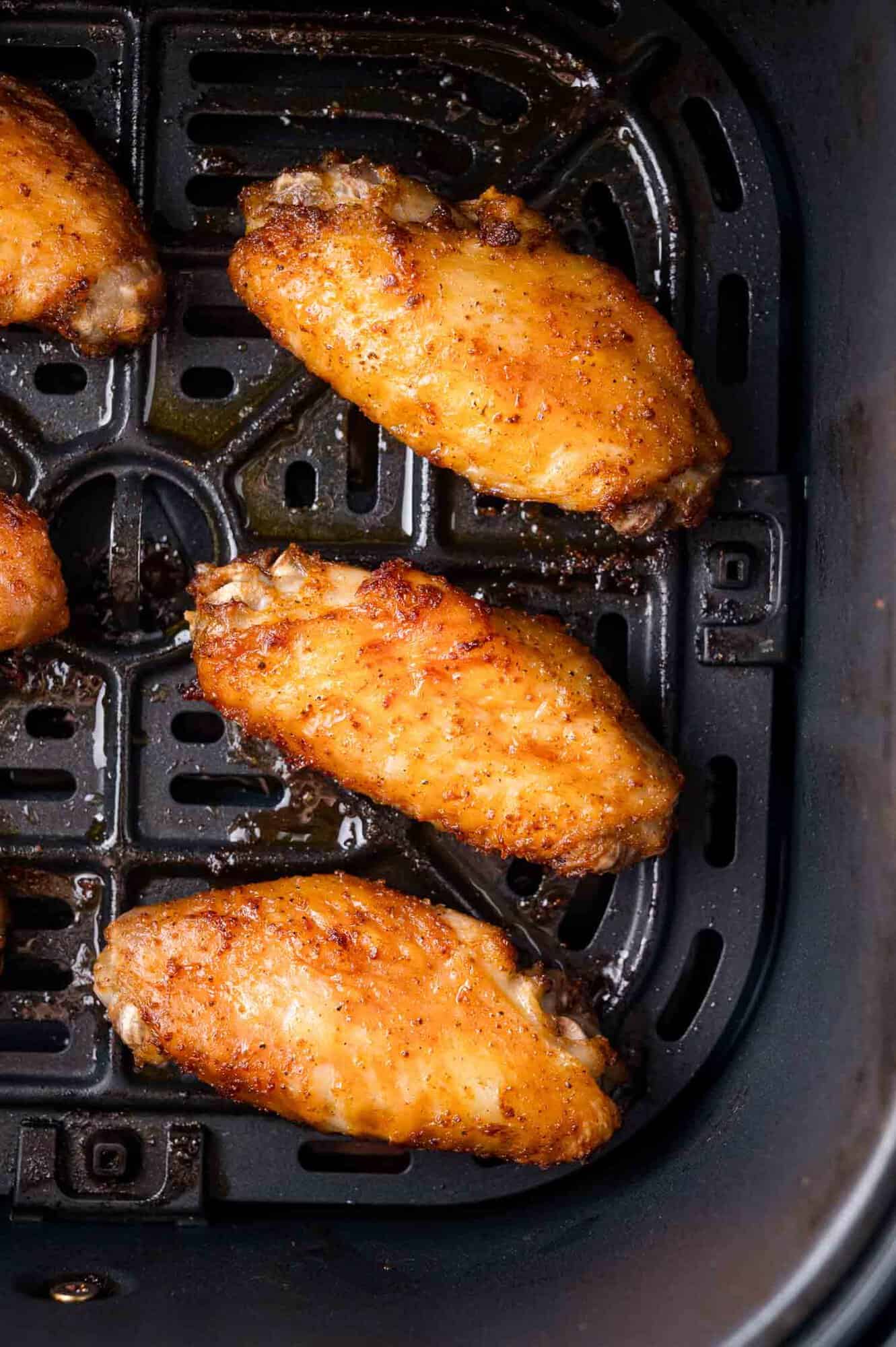 Four cooked chicken wings seasoned with spices are arranged in the basket of an air fryer.