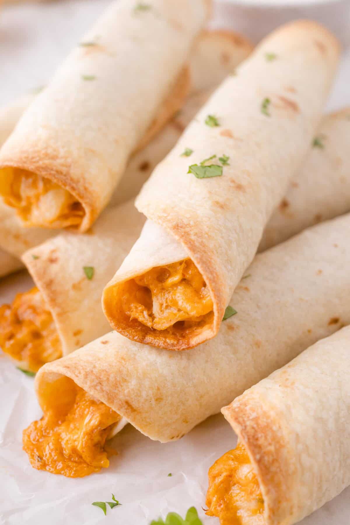 Five baked taquitos with melted cheese filling are arranged on parchment paper and garnished with chopped cilantro.