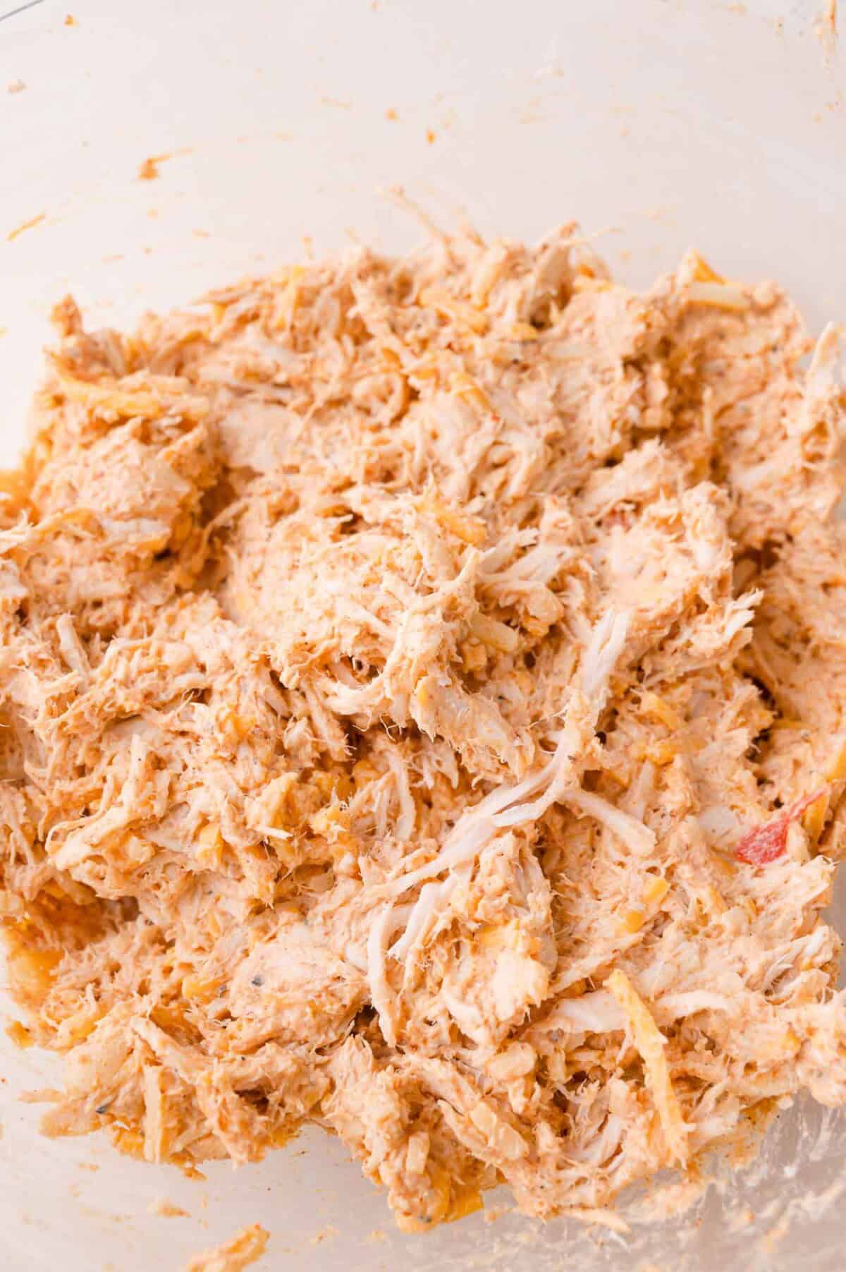 Shredded chicken mixed with spices and a creamy sauce in a clear glass bowl.