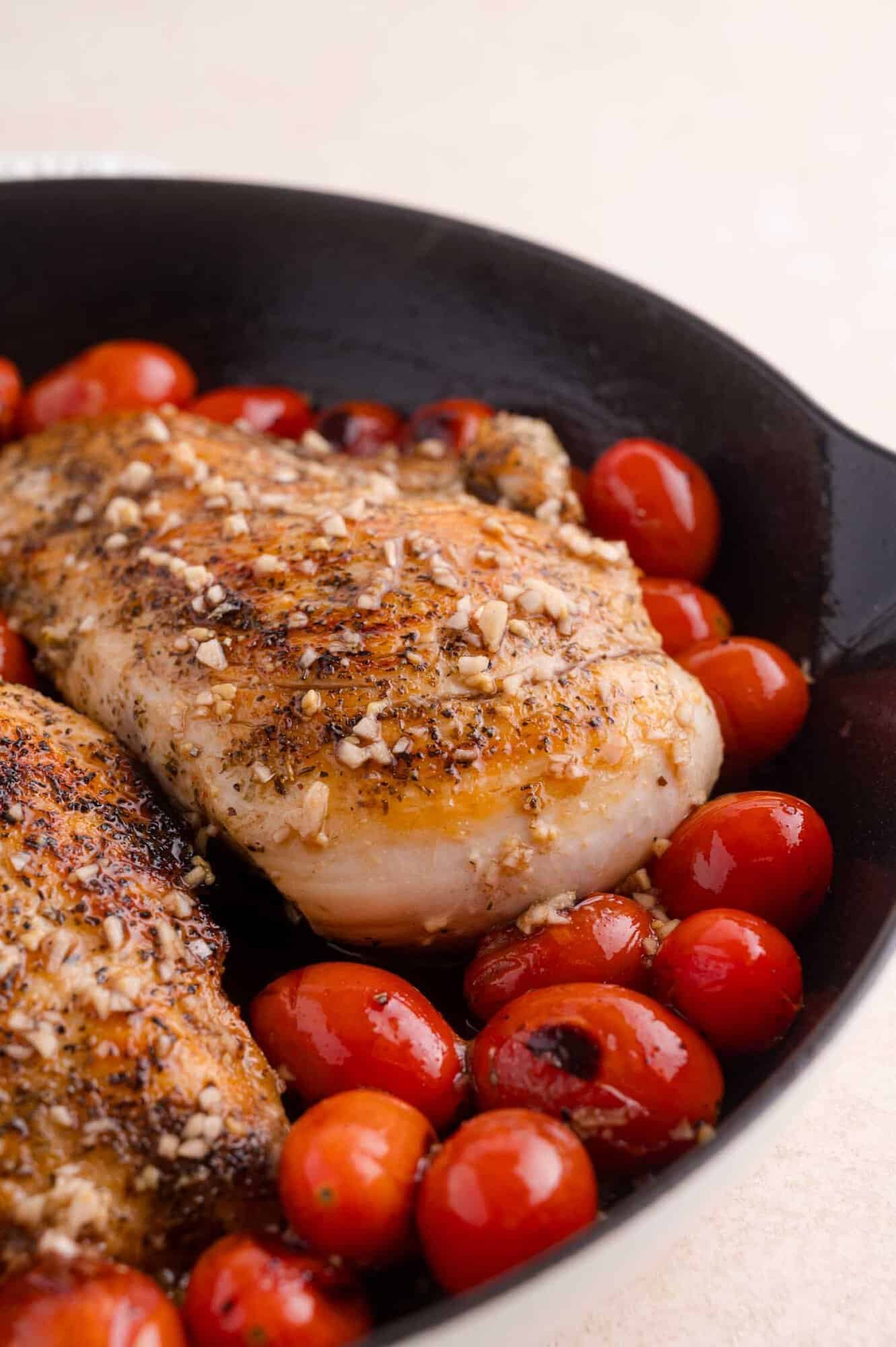 Seasoned chicken breast and cherry tomatoes in a black skillet.