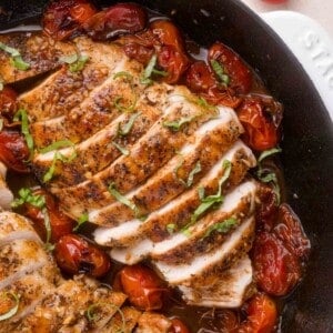 Sliced, seasoned chicken breast in a skillet with roasted cherry tomatoes and fresh basil garnish.