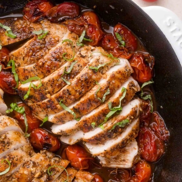 Sliced, seasoned chicken breast in a skillet with roasted cherry tomatoes and fresh basil garnish.