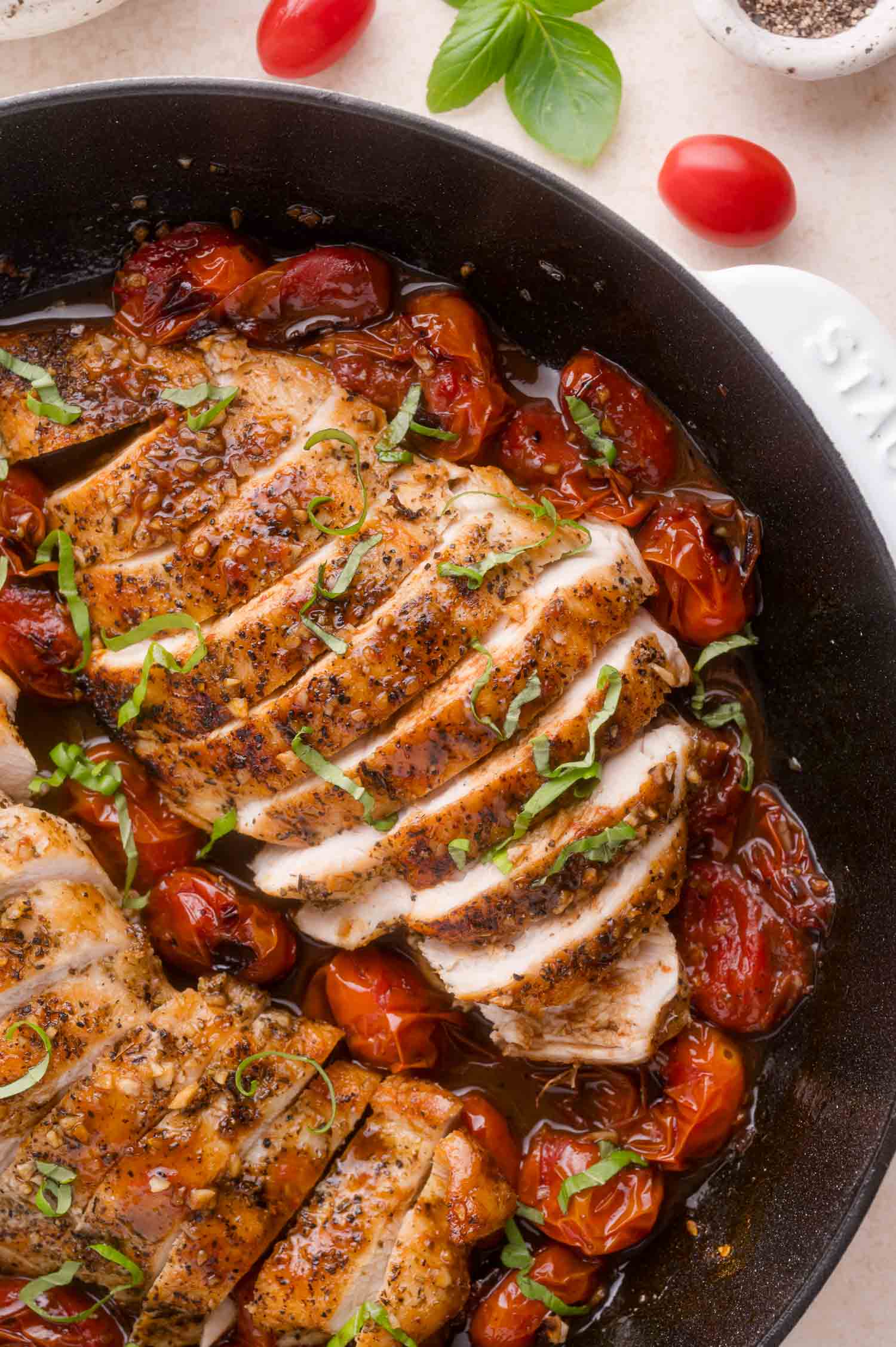 Sliced seasoned chicken breast in a skillet with roasted cherry tomatoes and fresh basil garnish.