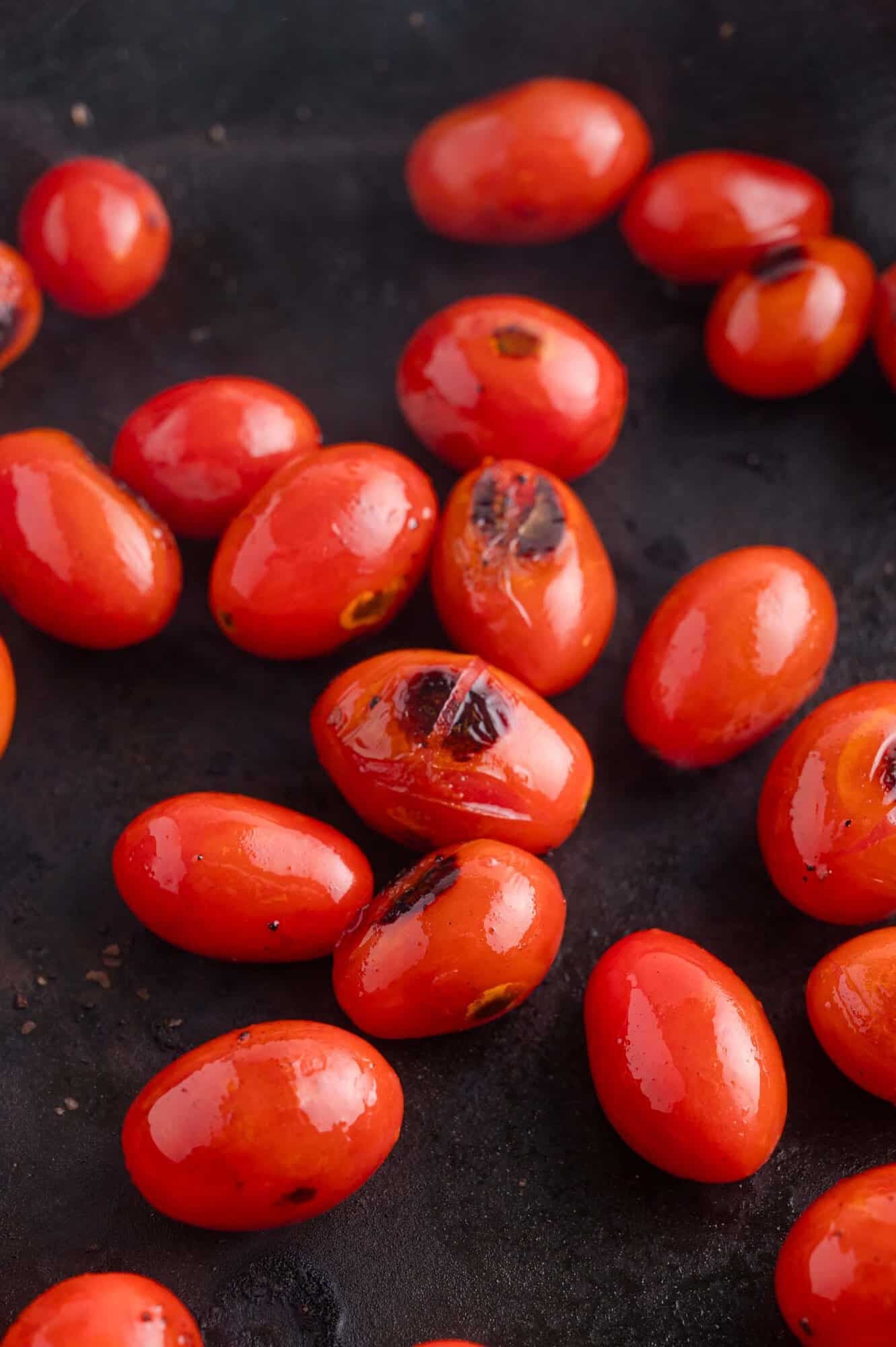 Several roasted grape tomatoes with charred spots are scattered on a dark surface.