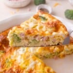 A close-up of a slice of broccoli, ham, and cheese crustless quiche being lifted from a pie dish.