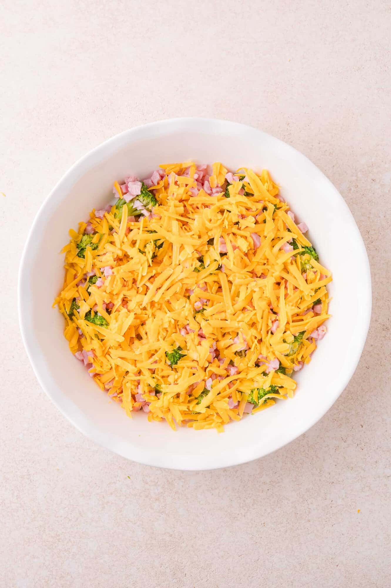 A white pie dish with cheese, broccoli, and ham.