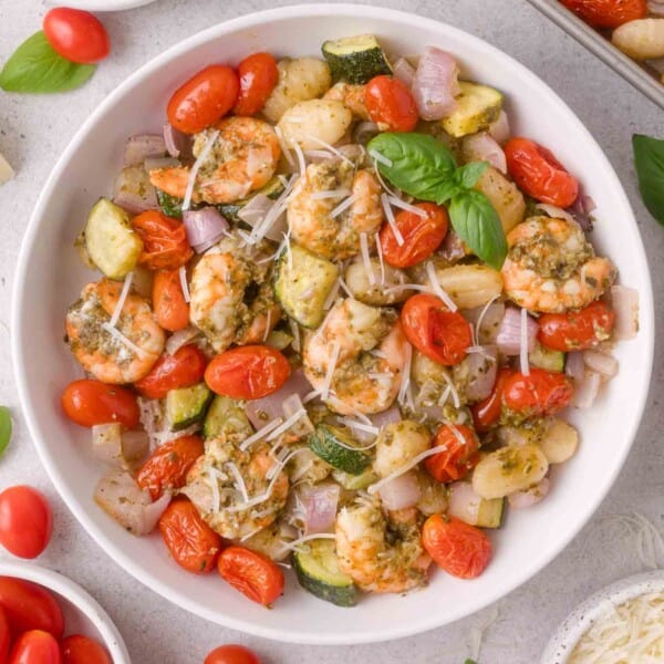 White bowl filled with gnocchi, shrimp, cherry tomatoes, zucchini, red onion, shredded cheese, and basil leaves.