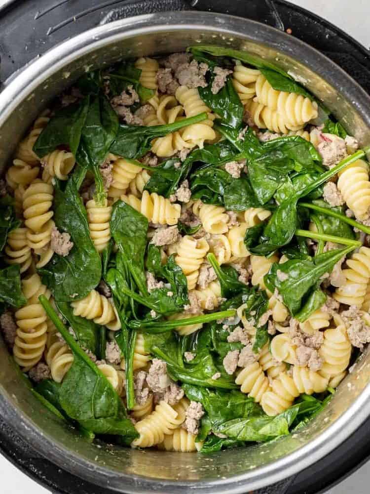 Spinach on top of ground chicken and pasta in an instant pot.