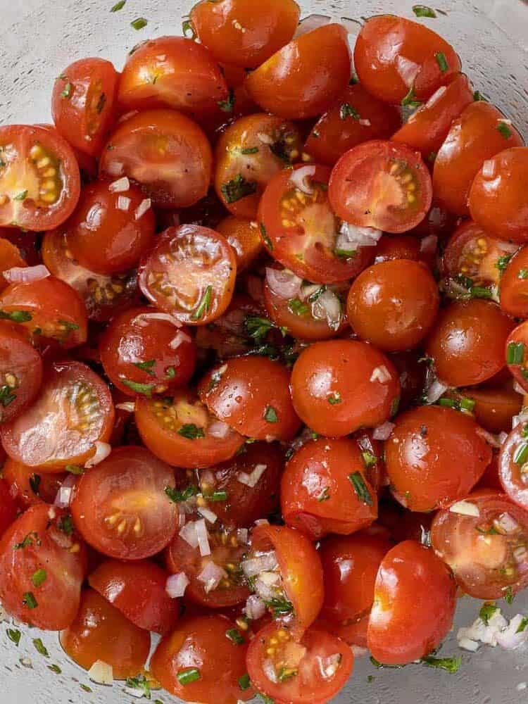 Tomatoes being marinated in a clear glass bowl.