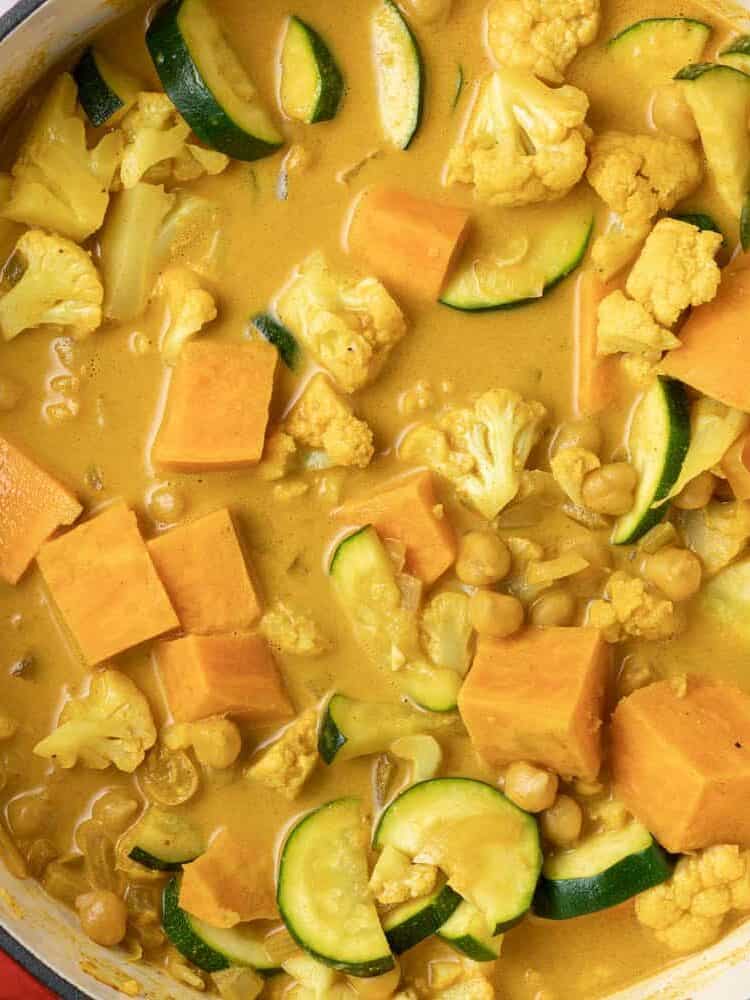 Uncooked vegetarian curry in a red dutch oven on a gray background.