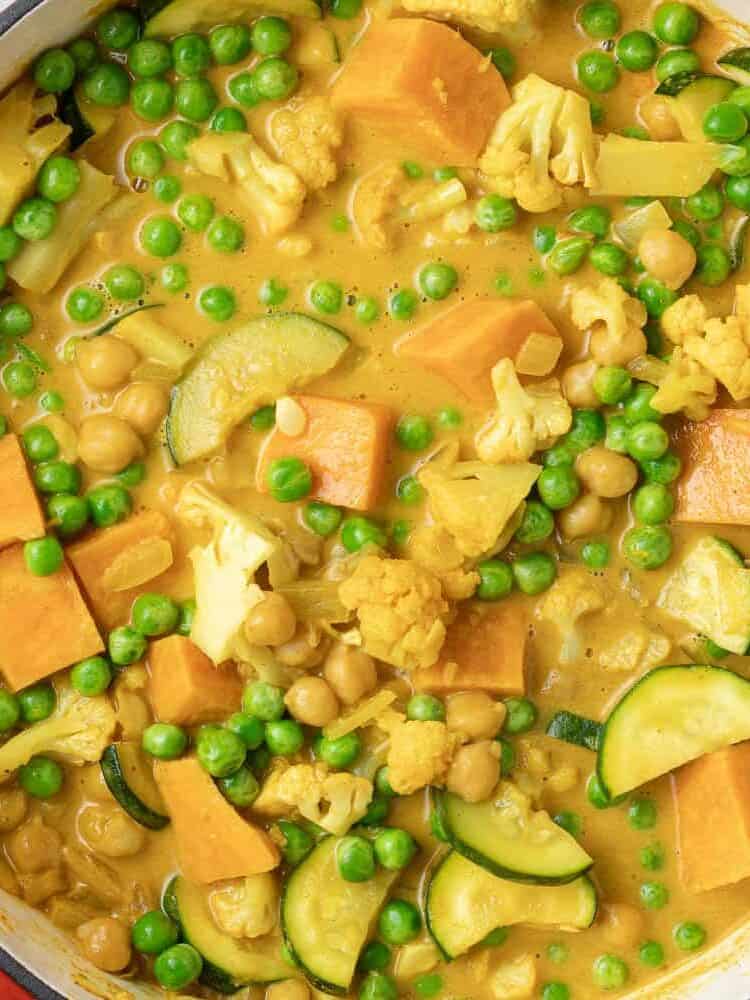 Peas added to a yellow orange curry in a red dutch oven.