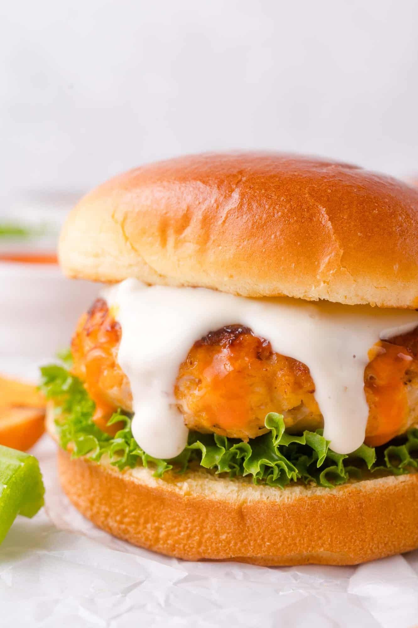 Buffalo chicken burger with lettuce and a thick layer of ranch on a soft bun, shown close up on a piece of parchment paper.