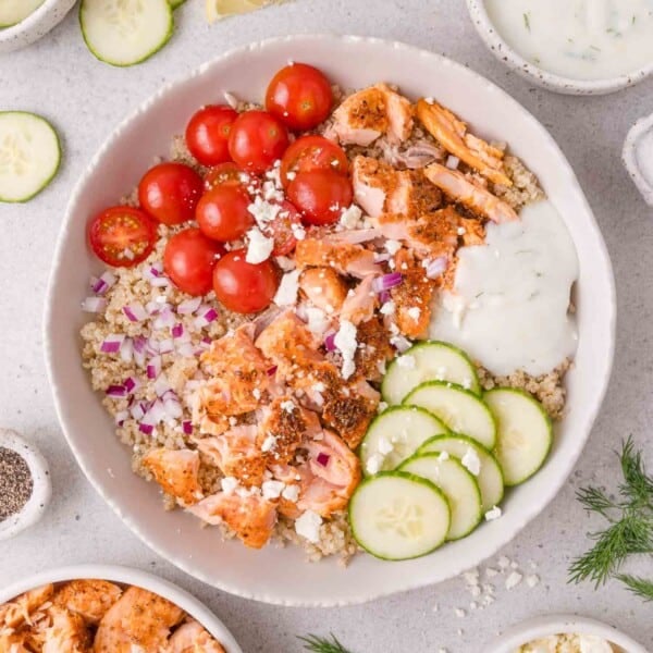 Bowl with quinoa, grilled salmon, cherry tomatoes, cucumbers, diced red onion, feta cheese, and tzatziki sauce.